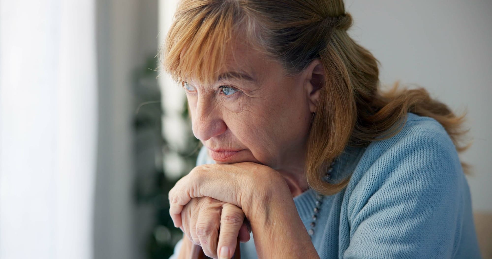 Femme d’âge mûr au regard pensif, appuyée sur ses mains, évoquant la fatigue et la douleur au quotidien.