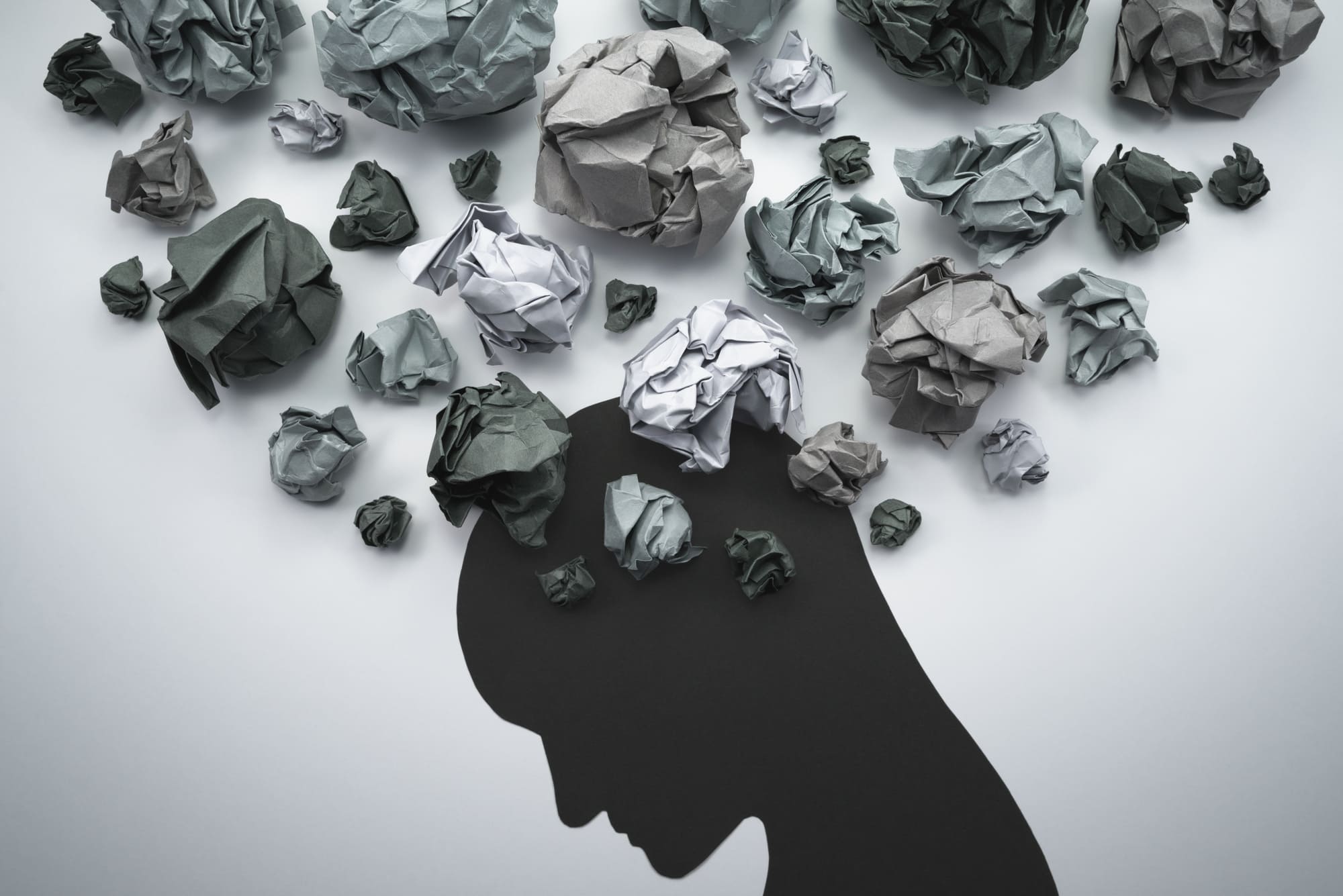 Silhouette d’une personne entourée de boules de papier froissé, symbolisant l’anxiété et les pensées envahissantes.