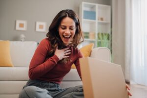 Femme souriante découvrant avec émotion un cadeau reçu chez elle