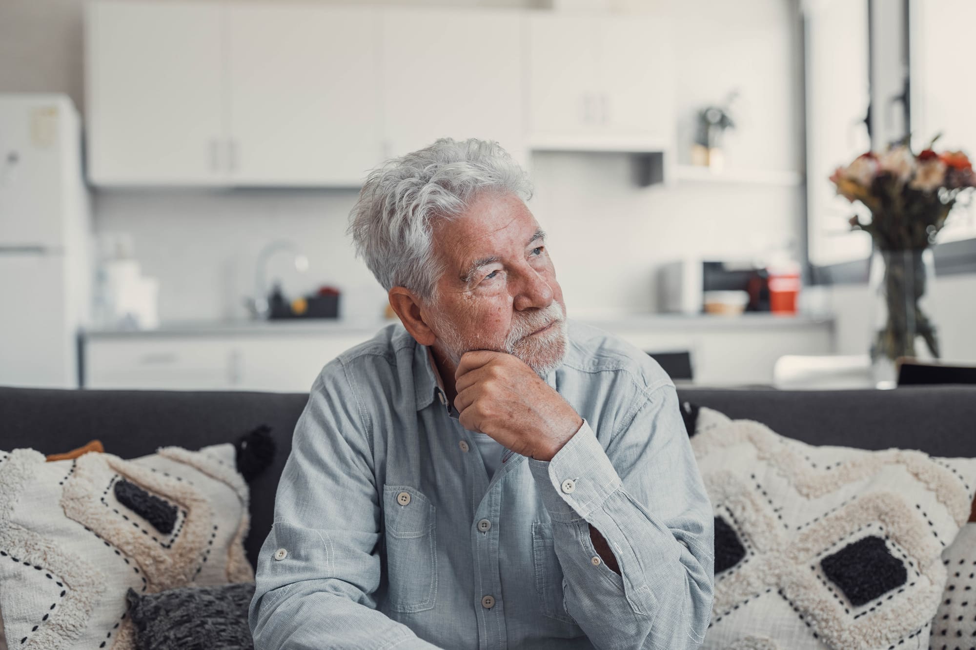 Homme âgé assis seul sur un canapé, le regard pensif, évoquant un sentiment d’impuissance et de culpabilité.