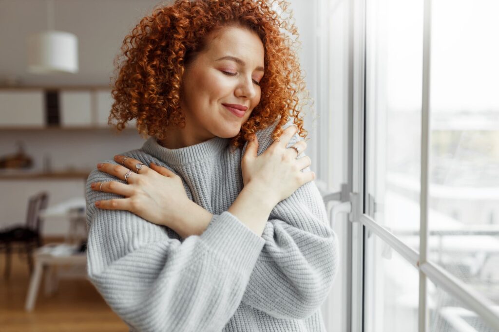 Femme aux cheveux roux se prenant dans ses bras, illustrant l’estime de soi et la bienveillance envers soi-même.