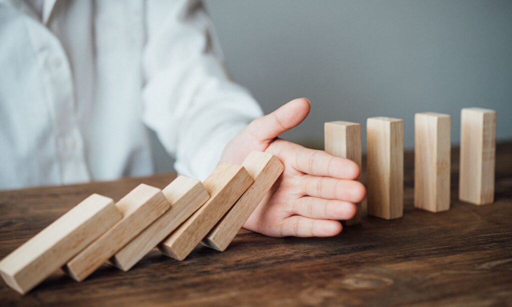 Main arrêtant la chute de dominos en bois, symbolisant la gestion des conflits et la prévention des difficultés relationnelles.
